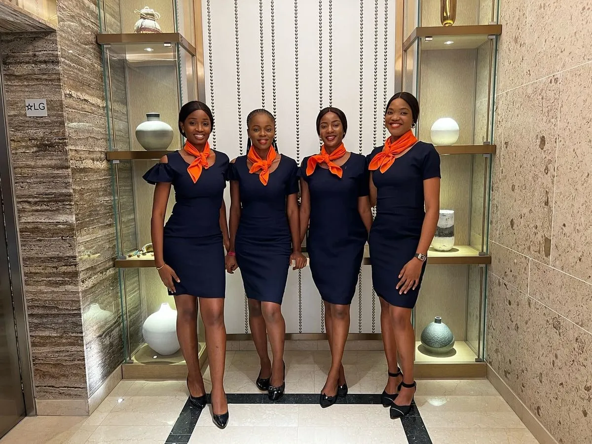 Four Anara ushers in navy dresses and orange scarves smiling in a hotel lobby