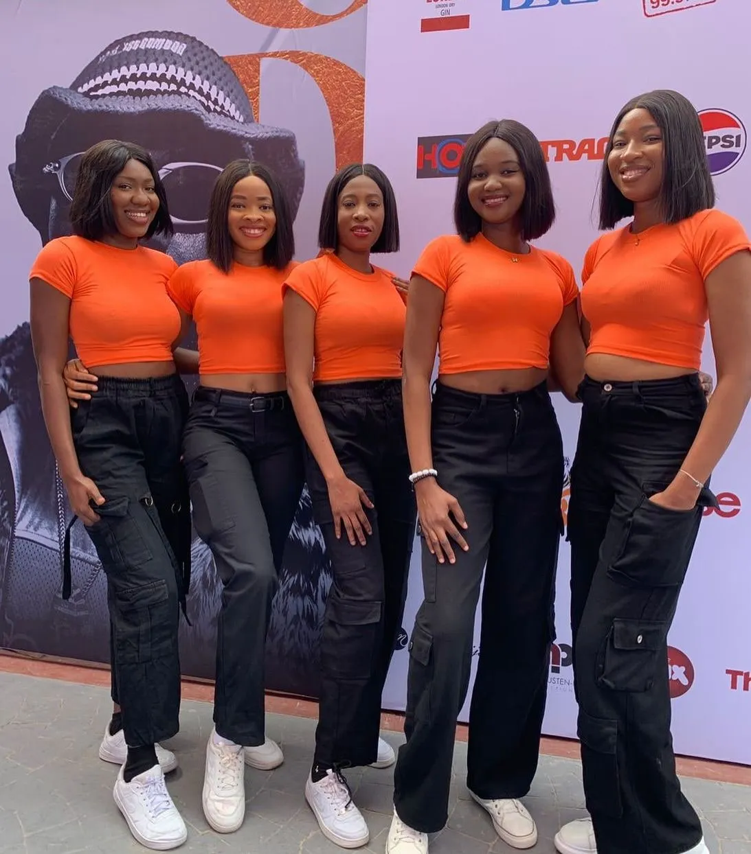 Five Anara ushers in matching orange tops and black trousers at a concert event